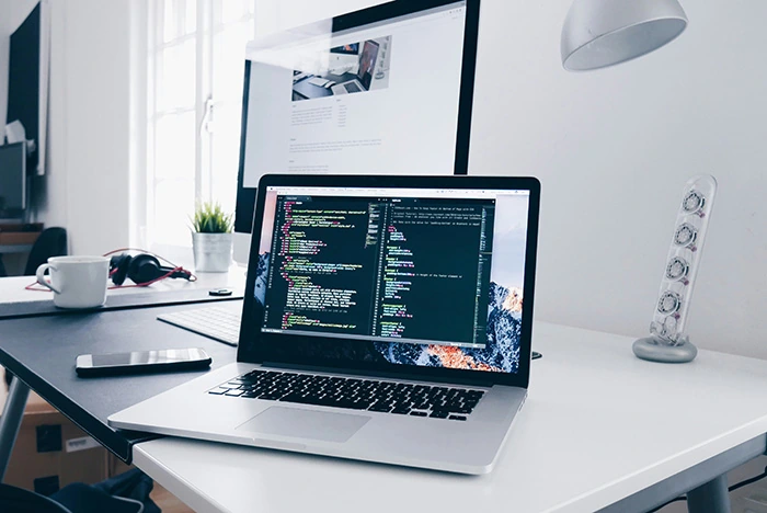 Desk with a laptop and monitor showing code related to Blockchain and Web3 QA Services